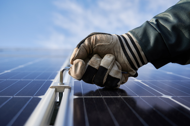 Close-up snapshot of a man's hand wearing a working glove, holding a hex key, installing solar module